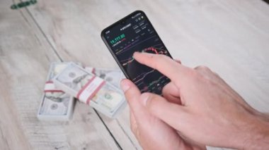 Yatırımcı akıllı telefon ekranındaki kripto para birimini kontrol ediyor. Masanın üstündeki telefon ekranında dolarlarla kripto ticareti. İşadamı, dijital borsa yatırımlarını inceliyor. Bitcoin fiyatı BTC Pazarı