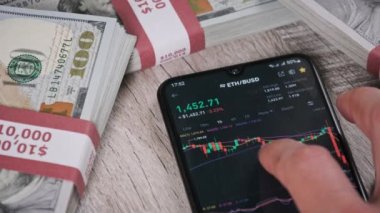 Yatırımcı akıllı telefon ekranındaki kripto para birimini kontrol ediyor. Telefon ekranında şifreli işlem masasında dolarlarla. İşadamı, dijital borsa yatırımlarını inceliyor. Ethereum fiyatı ETH Pazarı