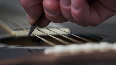 Yavaş çekimde akustik gitarda tellerin titreşimi. Klasik gitar metal telleri arabulucuya dokunurken titreşir. Slow Movement 240 fps, yakın çekim gitar destesi. Gitarist bronz tellere dokundu