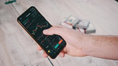 Yatırımcı akıllı telefon ekranındaki kripto para birimini kontrol ediyor. Masanın üstündeki telefon ekranında dolarlarla kripto ticareti. İşadamı, dijital borsa yatırımlarını inceliyor. Bitcoin fiyatı BTC Pazarı
