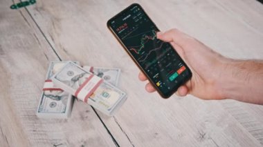 Şifreli akıllı telefon ticareti. İşadamı, dijital borsada dolarlarla dolu bir masanın üstündeki kripto fiyat tablosunu kontrol ediyor. BTC fiyatı. Kripto para ticareti. Çevrimiçi piyasa, değişim grafiği, Bitcoin