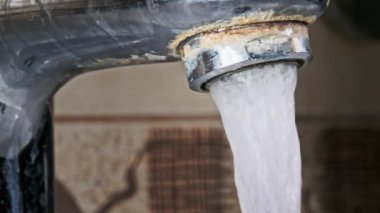 Ağır çekimde akan suyla musluk, makro çekim. Kirlenmiş eski bir musluktan kalsiyum ve kirle dolu bir su fışkırarak banyodaki bir lavaboya akıyor. Su açılıp kapanıyor. Yakın plan..