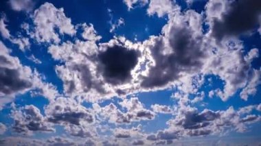 Mavi gökyüzünde, parlak güneşin altında hareket eden bulutlar, hızlandırılmış zaman. Bulut uzayı arka planı. Muhteşem cennette hafif kabarık bulutların zamanı. Manzaralı atmosfer. Hava değişikliği. Doğa. 4K