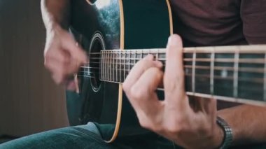 Gitarist evde akustik gitar çalar. Adam perdeleri tıngırdatır ve şarkıyı çalar. Klasik gitar çalmayı öğreniyorum. Genç müzisyen evdeki oturma odasında gitar çalıyor..
