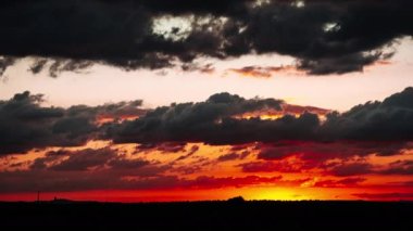Gün batımından sonraki bulutların zamanı turuncu renkli gökyüzünde hareket ediyor. Canlı, altın renkli alacakaranlık bulutları. Günbatımında koyu renkli bulutlar parlarken manzara hızlandırılmış kırmızı ve turuncu gökyüzü