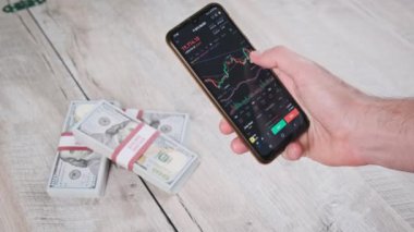 Şifreli akıllı telefon ticareti. İşadamı, dijital borsada dolarlarla dolu bir masanın üstündeki kripto fiyat tablosunu kontrol ediyor. BTC fiyatı. Kripto para ticareti. Çevrimiçi piyasa, değişim grafiği, Bitcoin