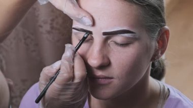 Building the shape of the eyebrows. Beauty salon. Eyebrow master dyes them for a young woman. Eyebrow correction and tint procedure. Girl sits with natural brown henna on brows. Close-up face. 4K