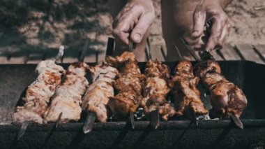 Grilling shashlik on barbecue grill outdoors. Process of cooking delicious shish kebab on a metal skewer in summer. Roast beef on BBQ. Marinated kebab grilled on charcoal. Weekend picnic. Street food