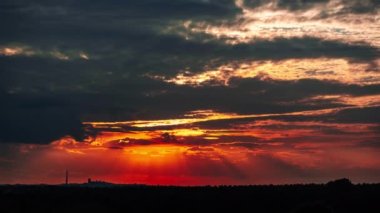Dramatic sunset with sun rays in the Sky through orange layered clouds, Timelapse. The big bright orange sun with sun rays moves down over the horizon. Awesome epic cloud space. Time Lapse. Sundown
