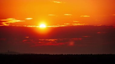 Timelapse of dramatic sunset with sun rays in the Sky through orange layered clouds. The big bright orange sun with sun rays moves down over the horizon. Awesome epic cloud space. Time Lapse. Sundown
