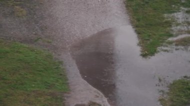 Sonbahar sokağındaki çamurlu su birikintilerine yavaş çekimde yağmur damlaları düşer. Yağmur damlaları kırsal alanda yere düşer. Yağmurlu sonbaharda kırsal yol
