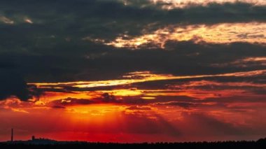 Dramatic sunset with sun rays in the Sky through orange layered clouds, Timelapse. The big bright orange sun with sun rays moves down over the horizon. Awesome epic cloud space. Time Lapse. Sundown