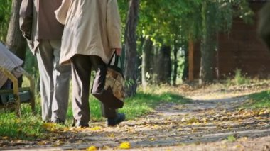Yaşlı emekliler bir sonbahar parkında yavaş çekimde, arka planda el ele yürürler. Birlikte yürürken el ele tutuşan yaşlı çift. Yaşlılıkta romantik bir çift. Aşk, sağlık, bakım, yaşam tarzı kavramları
