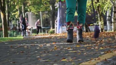 Kapıcı parkta düşmüş sarı yaprakları süpürüyor. Süpürgeyle süpürülen insanlar sonbahar parkında kaldırım taşlarının üzerinde yapraklar süpürüyor. Elektrik işçisi yeşillik topluyor. Güneşli sonbahar havasında temiz bölge..