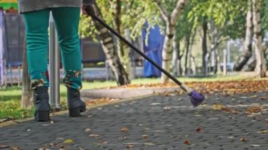 Kapıcı parkta düşmüş sarı yaprakları süpürüyor. Süpürgeyle süpürülen insanlar sonbahar parkında kaldırım taşlarının üzerinde yapraklar süpürüyor. Elektrik işçisi yeşillik topluyor. Güneşli sonbahar havasında temiz bölge..