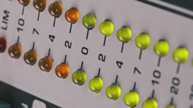 Vertical video LED indicator of sound level signal on mixing console. Close-up shot of strip in green and yellow on VU output level indicator. Volume level changes of indicator bulbs. Stereo meters