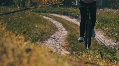Güneşli bir yaz gününde yeşil orman yolunda bisiklet süren genç bir kadın. Ağır çekim. Bisikletli bir kadın kırsalda yeşil çimlerin çok yakınında patikaya çıkıyor. Sağlıklı bisiklet yaşam tarzı, boş zaman aktivitesi.