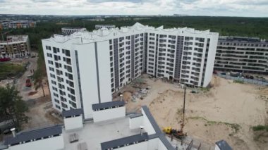 Orman bölgesindeki yeni ve çok katlı bir binanın havadan görünüşü. Yüksek bir binanın dış tarafında uçuyorlar. Geniş camlı balkonları ve beyaz cepheli yeni inşa edilmiş dairenin modern tasarımı..
