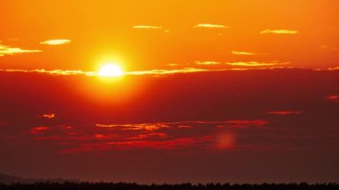 Timelapse of dramatic sunset with sun rays in the Sky through orange layered clouds. The big bright orange sun with sun rays moves down over the horizon. Awesome epic cloud space. Time Lapse. Sundown