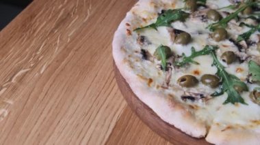 Restorandaki ahşap bir masada iştah açıcı pizza. Erimiş peynir, zeytin, mantar ve bitkilerin yakın plan çekimi. Tahtada yeni pişmiş peynirli pizza. İtalyan mutfağı. 4K