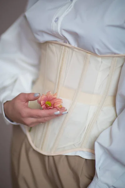 Beyaz gömlekli ve bej korseli kız ellerinde çiçekler tutuyor.