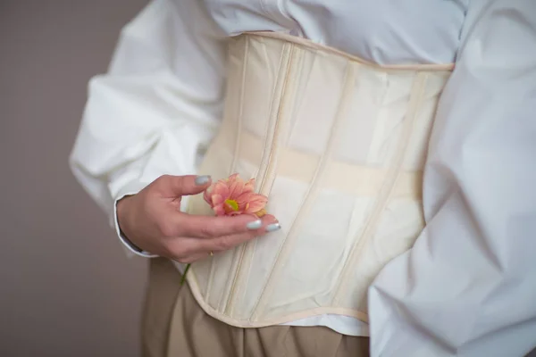 Beyaz gömlekli ve bej korseli kız ellerinde çiçekler tutuyor.