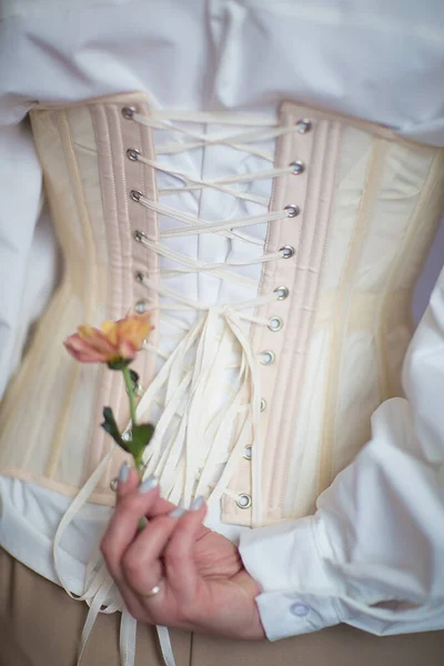 Beyaz gömlekli ve bej korseli kız ellerinde çiçekler tutuyor.