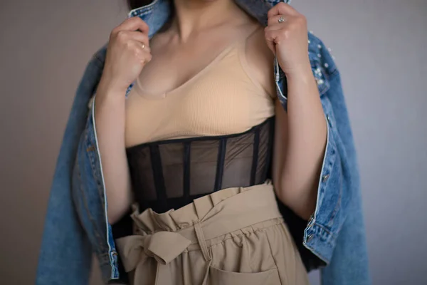 Bej bluzlu kız, korse, pantolon ve kot ceketli.