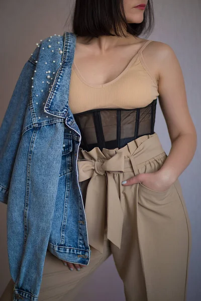 Bej bluzlu kız, korse, pantolon ve kot ceketli.