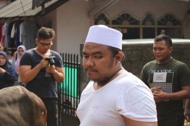 Jakarta, Endonezya - 12 04 2020: Şapkalı ve beyaz gömlekli bir adam başka tarafa bakıyordu ve arkasında bir kalabalık vardı.