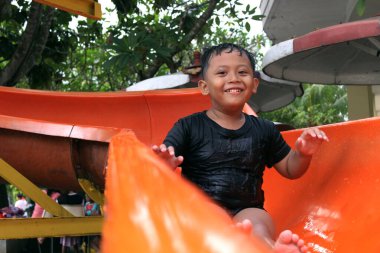 Tangerang, Endonezya - 11 19 2020: Yüzme alanında slayt çalan ve mutlu görünen bir çocuk