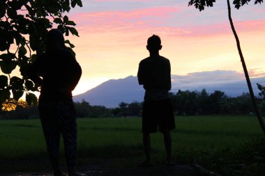 Java, Endonezya - 12.14 2020: Şafak vakti gökyüzü hala turuncu olan doğal manzaraya bakan insanlar