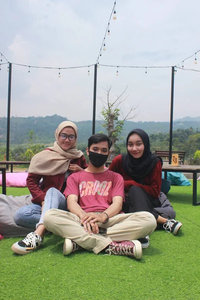 Bogor, Endonezya - 09-10-2020: Türbanlı iki kadın ve kırmızılı bir erkek Rainbow Hill Kafe 'nin avlusunda oturuyorlar, Bogor, Batı Java