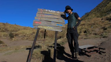 Magelang, Endonezya - 08 06 2019: açık mavi bir gökyüzünün arka planına tırmanırken bir tabelanın yanında duran bir adamın ifadesi