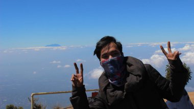 Magelang, Endonezya - 06 08 2019: Merbabu Dağı 'na tırmanırken gökyüzüne karşı poz veren adam, Magelang, Merkez Java