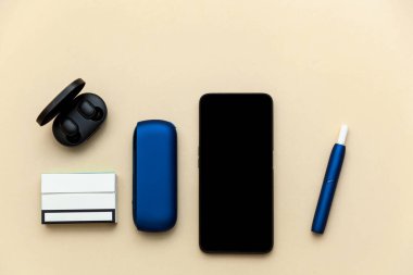 Elektronik mavi IQOS sigara, telefon, bej arka planda kulaklık. Metnin, logon ve tasarımın için bir fotoğraf. Danışma ofisi.