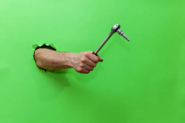 Man holds hand tool for fixing plumbing on green background