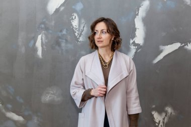 Yeşil külotla poz veren şık ve şık bir kız, gri bir duvara karşı bir süveter ve açık renk bir ceket.