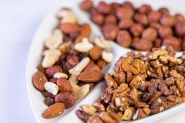 Beyaz ahşap bir masada beyaz bir tabakta çeşitli fındıklar..