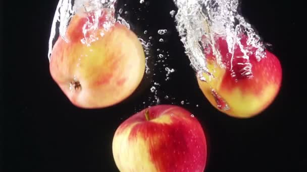 Reife Äpfel, die durch Wasser fallen. dunkler Hintergrund. Zeitlupe. — Stockvideo