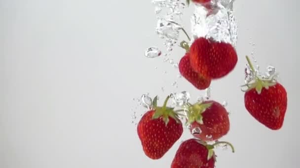 Reife Erdbeeren fallen durch das Wasser. Licht im Hintergrund. Zeitlupe. — Stockvideo