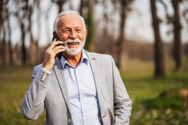 Mutlu kıdemli işadamı işten sonra dinleniyor. Akıllı telefondan konuşuyor..