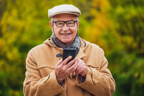 Открытый Портрет Веселого Пожилого Человека Зимнем Пальто Который Пользуется Смартфоном — стоковое фото