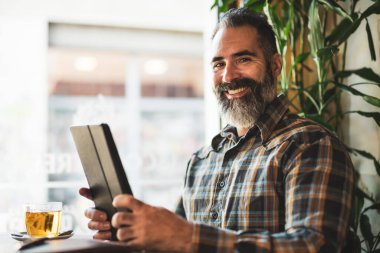 Yetişkin adam kafede oturuyor ve dijital tablet kullanıyor. Rahatlıyor..