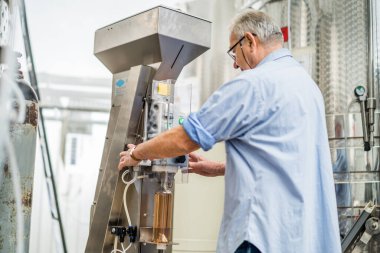 Kıdemli adam içki fabrikasındaki şarap şişesini tıkamak için makine kullanıyor..