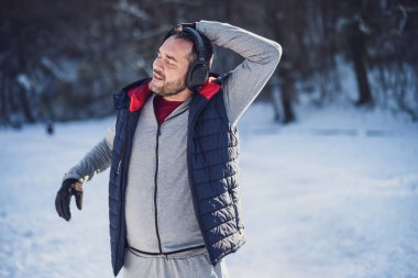 Yetişkin bir adam kışın parkta egzersiz yapıyor. Koşmadan önce vücudunu esnetiyor..