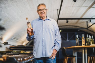 Şaraphane sahibi kıdemli bir adamın portresi. Şarap mahzeninde kaliteyi inceliyor. Endüstriyel şarap yapma kavramı.