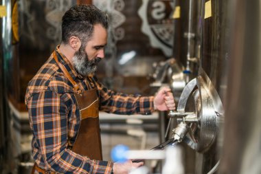 Man is working at craft beer factory. He is operating machinery in brewery. Small family business, production of craft beer.