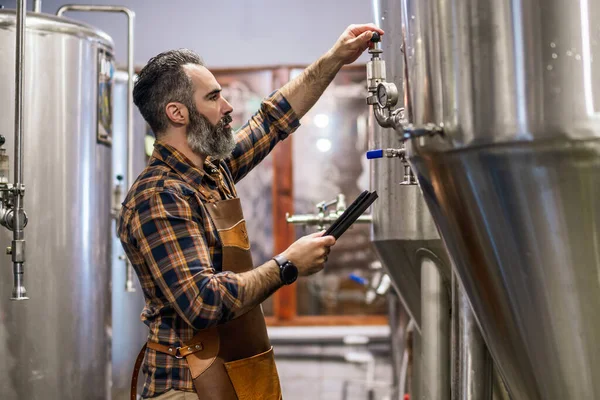 Man is working at craft beer factory. He is operating machinery in brewery. Small family business, production of craft beer.