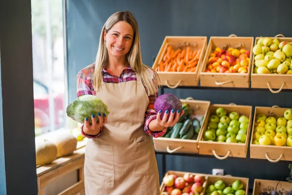 Woman works in fruits and vegetables shop. She is holding cabbage.